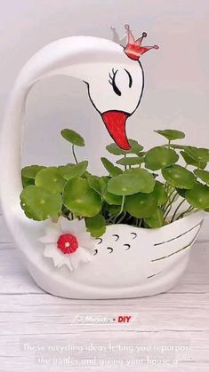 a white swan planter with green plants in it's mouth and a red crown on its head