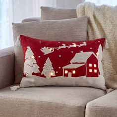 a red pillow with white christmas lights on it sitting on a couch next to a window