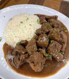 a white plate topped with meat and rice on top of a wooden table next to a fork