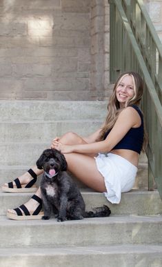 a beautiful young woman sitting on the steps with her black dog in front of her