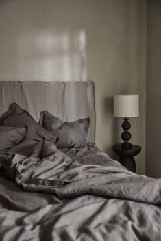 an unmade bed with grey sheets and pillows