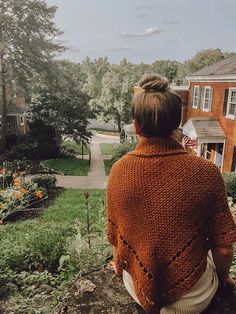 a woman sitting on top of a tree stump in front of a house and garden