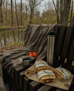 bread and oranges on a picnic table next to a lake with a blanket over it