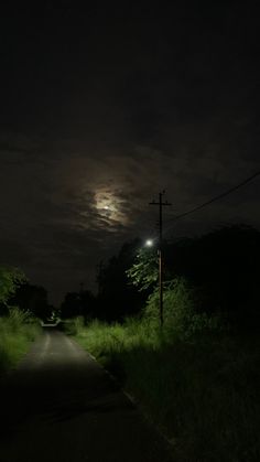 an empty road at night with the moon in the sky and grass on both sides