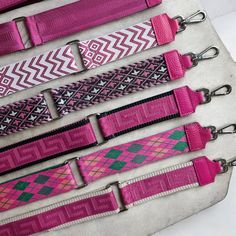 five pink and green belts are lined up on a white surface with black metal hooks