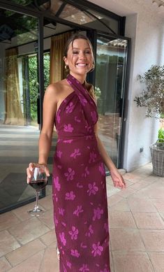 a woman in a purple dress holding a glass of wine and posing for the camera