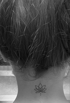 the back of a woman's neck with a small lotus tattoo on her left side