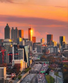 the sun is setting over a city with tall buildings and cars driving down the road