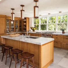 a large kitchen with wooden cabinets and marble counter tops, along with four stools