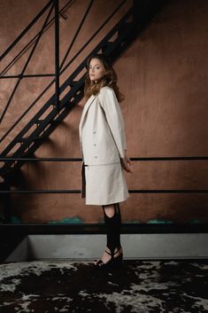 a woman in a white coat and black dress standing next to a stair case with her hands on her hips