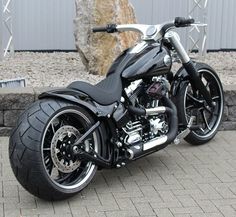 a black motorcycle parked on top of a brick road next to a stone wall in front of a building