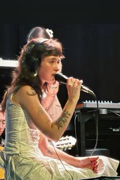 a woman sitting on top of a piano while holding a microphone