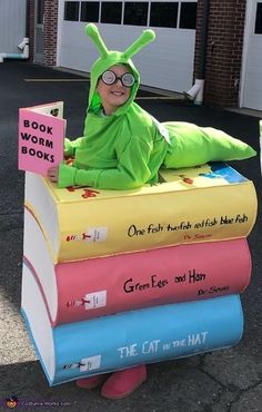 a child in a book worm costume sitting on top of books with a sign reading the cat in the hat