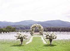 an outdoor ceremony set up with white flowers and greenery in vases on the grass