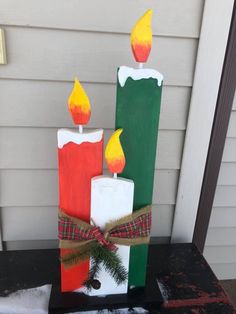 three candles are sitting on top of each other in front of a house with snow