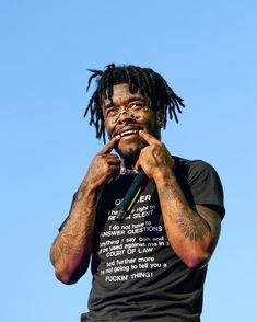 a man with dreadlocks on his face holding a microphone to his mouth while standing in front of a blue sky