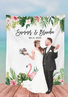 a couple posing for a wedding photo in front of a tropical themed beach backdrop with flamingos and palm leaves