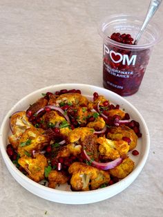 a white bowl filled with cauliflower and onions next to a cup of pomegranate