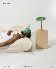 a woman laying on top of a white couch next to a green lamp and table