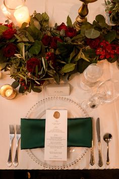 the place setting is set with silverware, napkins and red roses on it