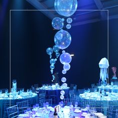 the tables are set up for an event with blue lights and clear balloons hanging from the ceiling