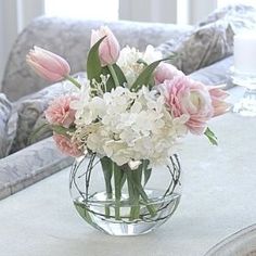 a glass vase filled with white and pink flowers on top of a table next to a couch