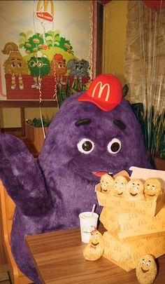 a large purple stuffed animal sitting on top of a wooden table next to a mcdonald's sign