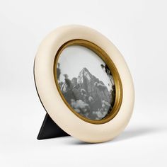 a white and gold frame with a mountain in the background on a black metal stand