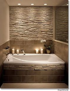 a bathtub with candles on the side and stone wall in the backround