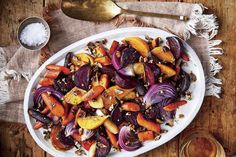 a white plate topped with roasted vegetables next to a glass of wine and spoons