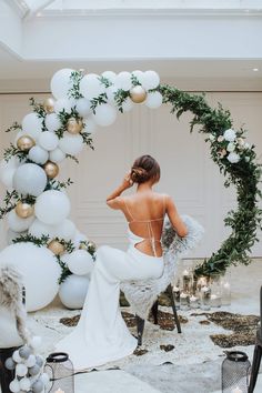 a woman sitting on a chair in front of a white arch with balloons and greenery