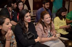 three women sitting next to each other at a social event with people in the background