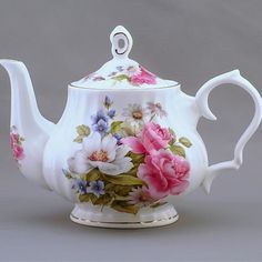 a white tea pot with flowers painted on the outside and inside, sitting on a gray surface