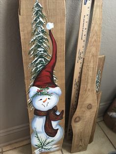 a wooden snowman with a red hat and scarf standing next to a ruler on the floor