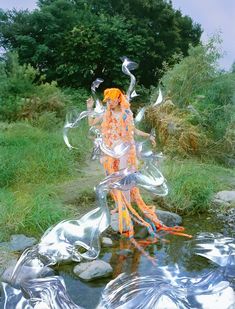 a woman with orange hair is standing in the water near some rocks and grass,