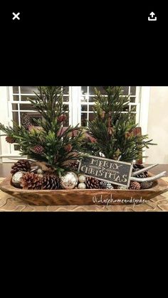 a wooden tray filled with pine cones and christmas decorations on top of a table next to a window