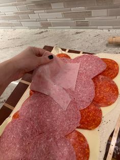 a person cutting up slices of salami on top of pizza