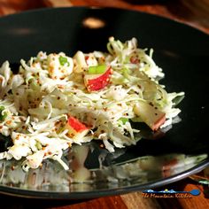 a black plate topped with coleslaw slaw covered in seasoning next to a wooden table