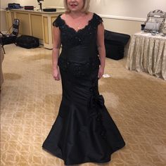 a woman in a black dress standing on a carpeted floor with a table behind her