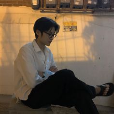 a man sitting on the ground with his feet crossed and wearing black pants, white shirt and black shoes