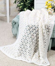 a white crocheted blanket sitting on top of a couch next to a potted plant