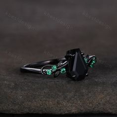 a black ring with green crystal stones on it's sides sitting on a rock