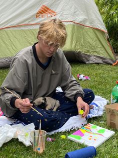 a young man sitting on the ground painting with paintbrushes and an easel