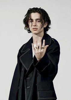 a young man in a black jacket making the v sign with his hand while standing against a white background