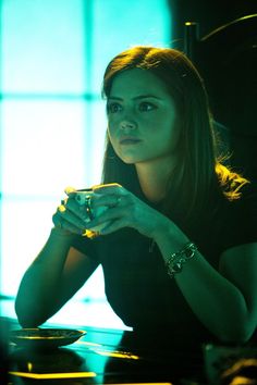 a woman sitting at a table with a cup in her hand and looking off into the distance