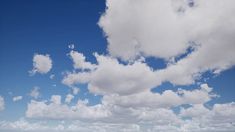 two people on the beach flying a kite under a cloudy blue sky with white clouds