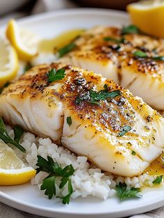 some fish and rice on a plate with lemon wedges, parsley and water