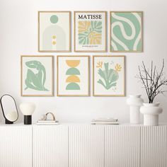 four framed art prints on the wall above a white credenza with vases