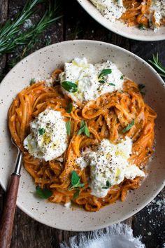 a white bowl filled with pasta and cheese on top of a wooden table next to herbs