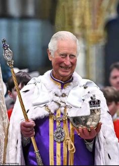 an older man dressed in white and purple holding two metal items with other people behind him